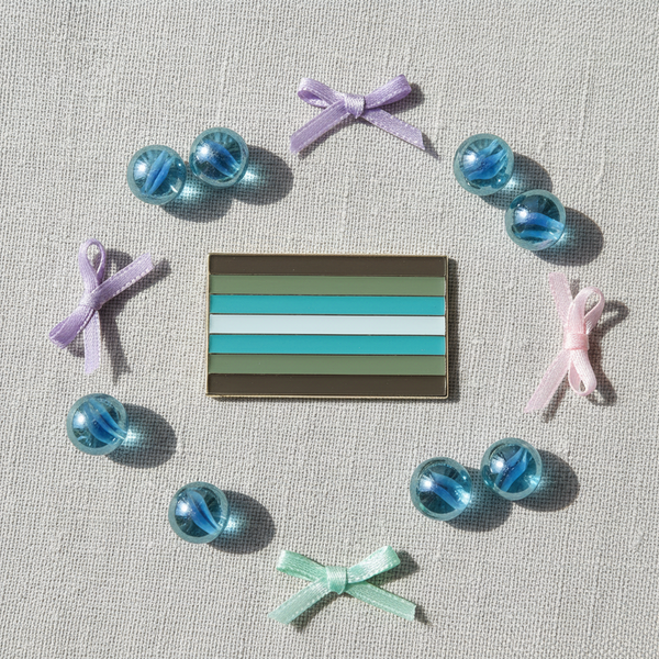 Rectangular demiboy flag enamel pin on fabric, surrounded by blue marbles and pastel bows