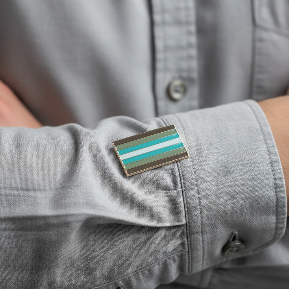 Close-up of a demiboy flag enamel pin with teal, gray, and white stripes on a shirt cuff