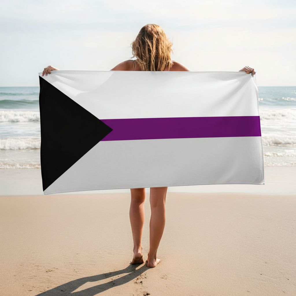 Demisexual Pride flag towel—black triangle left, purple stripe on white—held by barefoot person at ocean shore