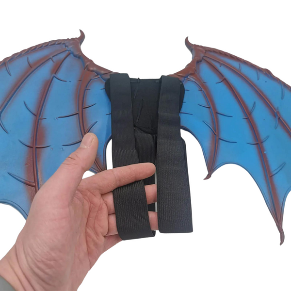 Back view of blue bat-like cosplay wings with black adjustable shoulder straps, held by a hand