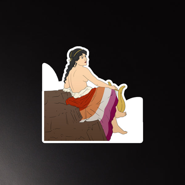 Illustrated magnet of a nude woman playing a lyre beside a rocky ledge