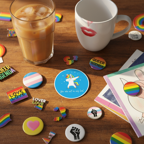 Blue unicorn “You are not on my level” magnet among queer-themed pins on a wooden table