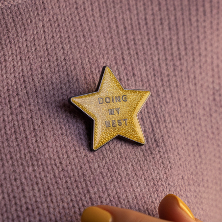 Gold star enamel pin reading “DOING MY BEST” on mauve knitted fabric