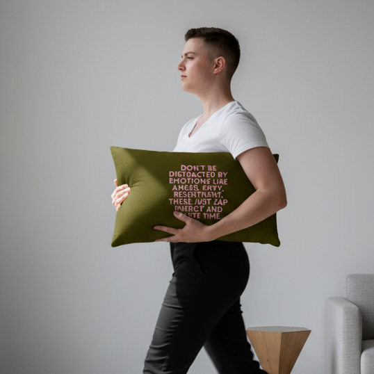 Short-haired person in white tee and dark pants holds “Dont Be Distracted By Emotions” pillow; pink and white text