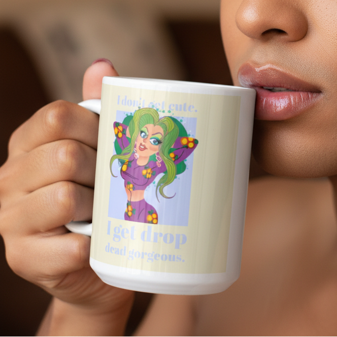 Person holding a white mug with a green-haired cartoon character and “I get drop dead gorgeous” text