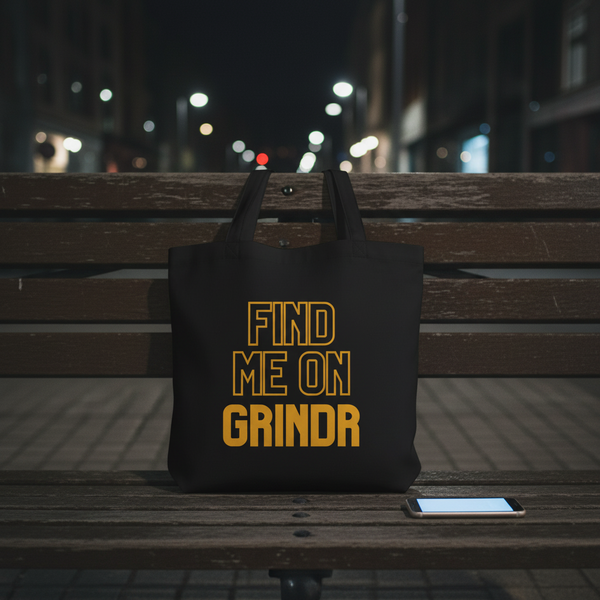 Eco tote bag with “Find Me On Grindr” in bold yellow on black, laid on a wooden bench at night next to a smartphone.