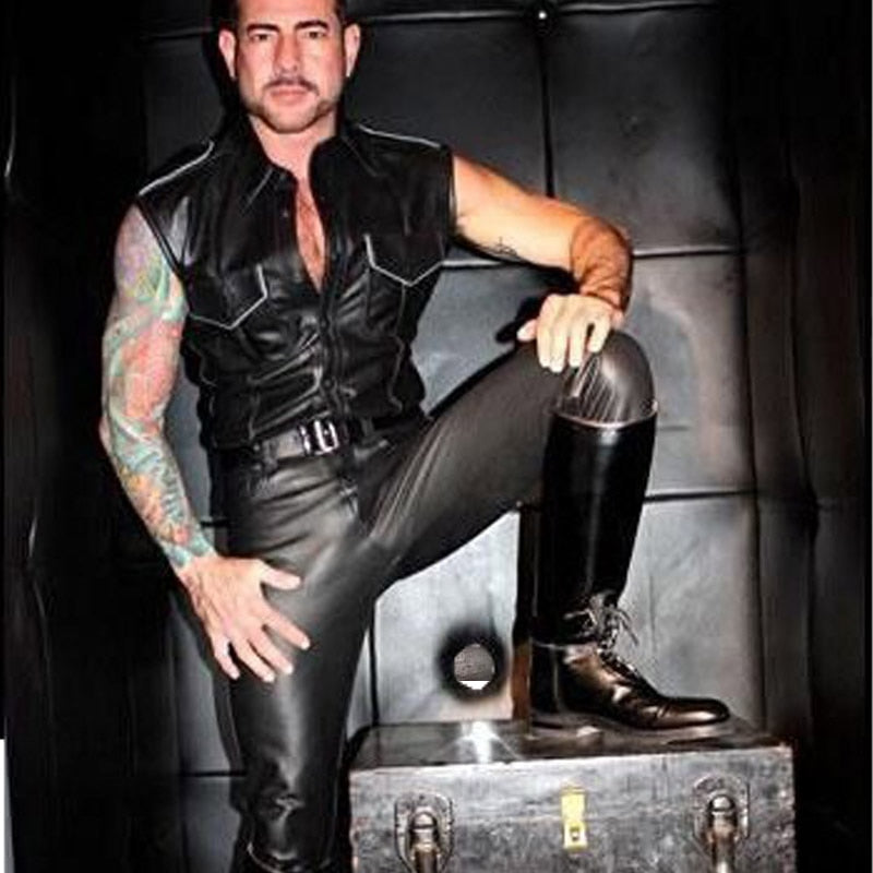 Tattooed person modeling tight black faux-leather pants while seated on a trunk