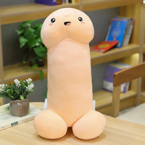 Front-facing peach penis-shaped plush pillow with a cute embroidered face on a table