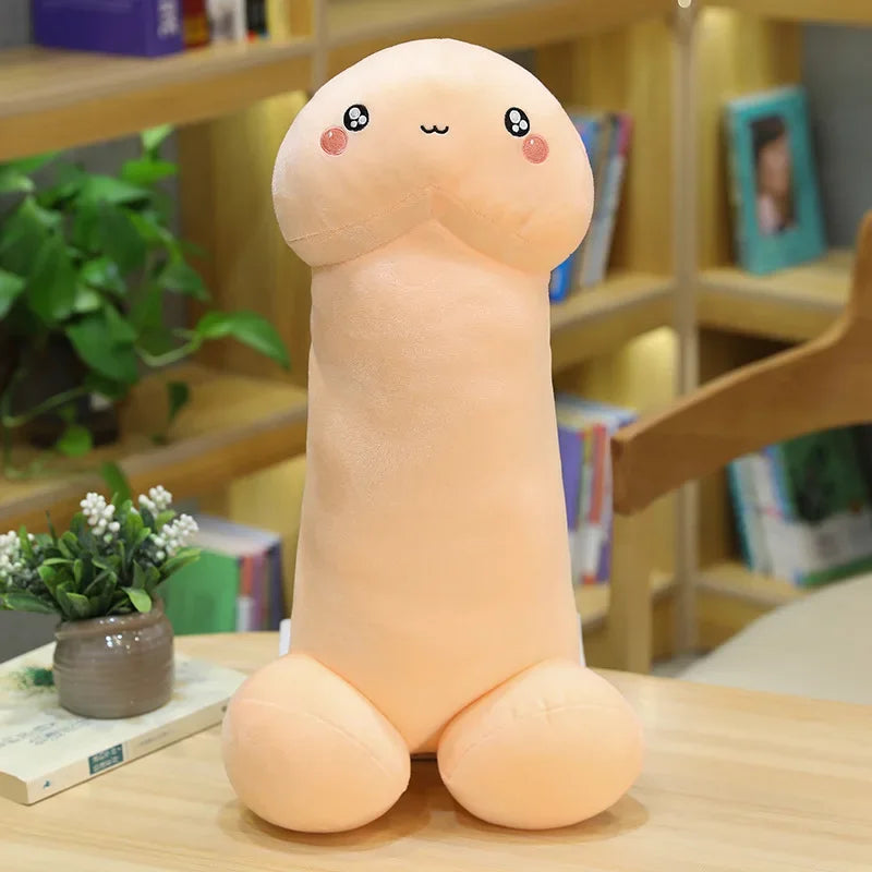 Peach-colored penis-shaped plush pillow with a cute embroidered face, seated on a table