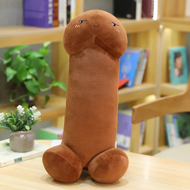 Brown penis-shaped plush pillow with a worried embroidered face, seated on a table