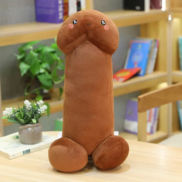 Brown plush penis-shaped pillow with a cute face and rounded feet on a table