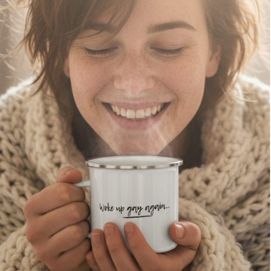 “Woke up gay again…” slogan on a white enamel mug held by a smiling person