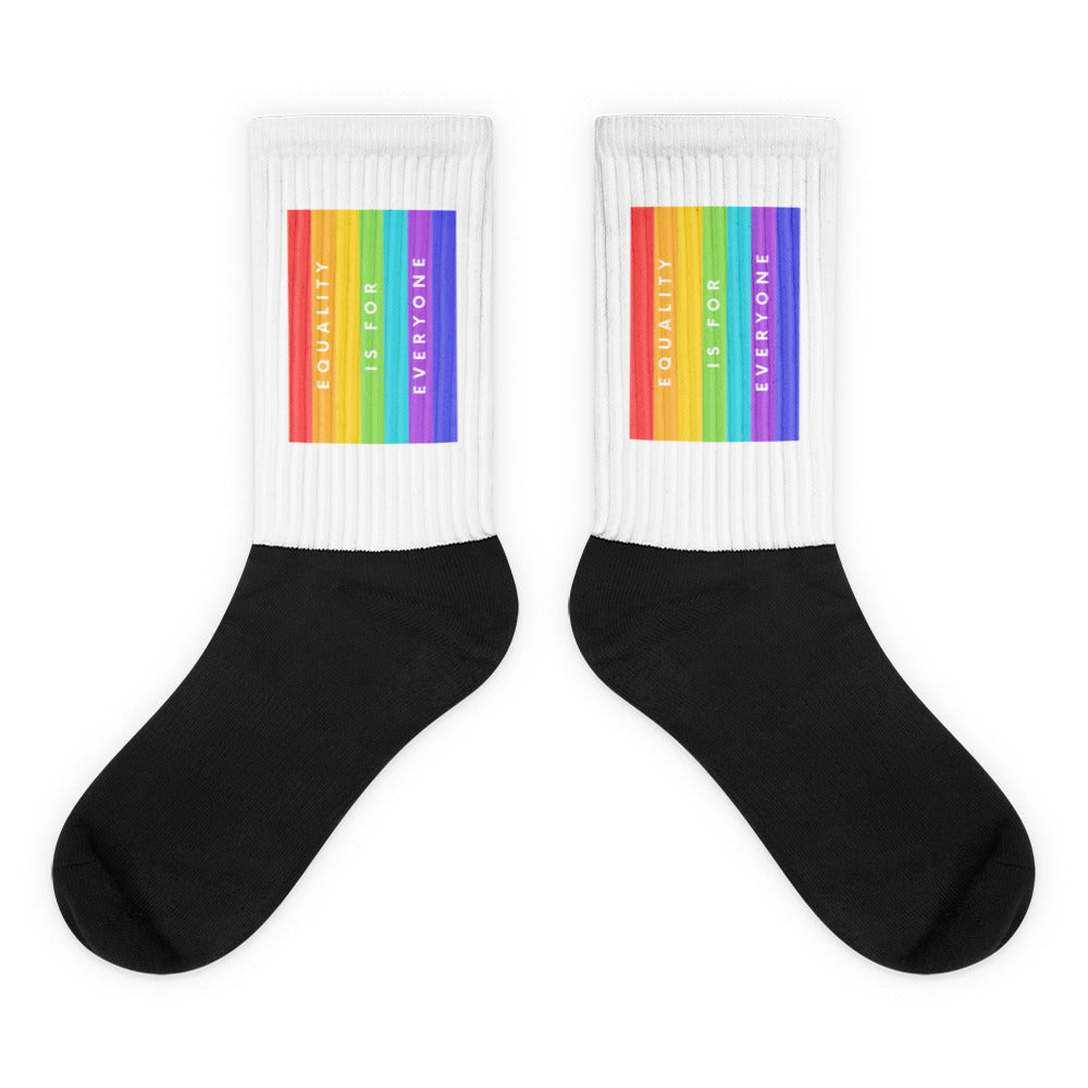 Pair of black-and-white socks with rainbow bands reading “EQUALITY IS FOR EVERYONE”