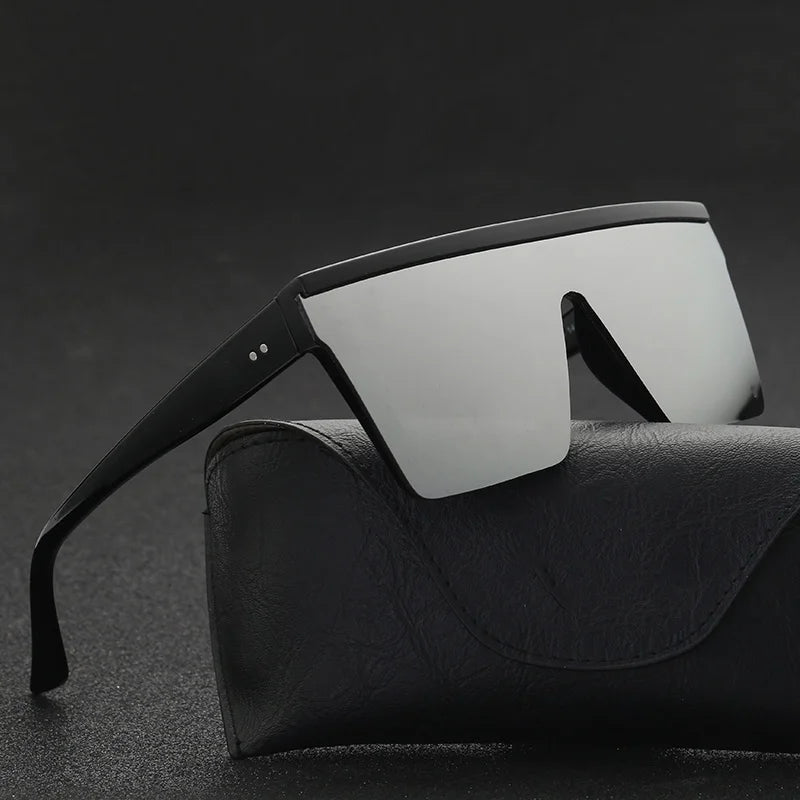 Black oversized shield sunglasses resting diagonally on a black textured case