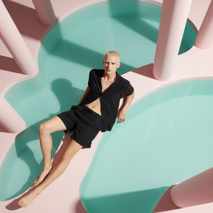 Black short-sleeve shirt and matching drawstring shorts worn by a model beside a pastel pool