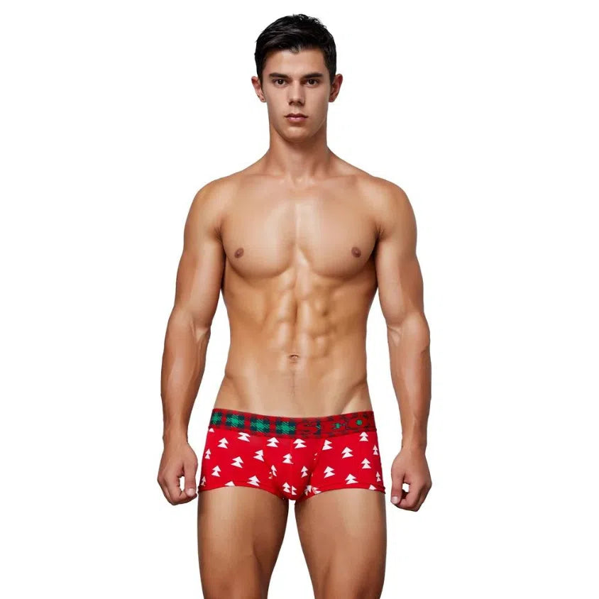 Front-facing shirtless model wearing red boxer briefs with white tree motifs and a green tartan waistband