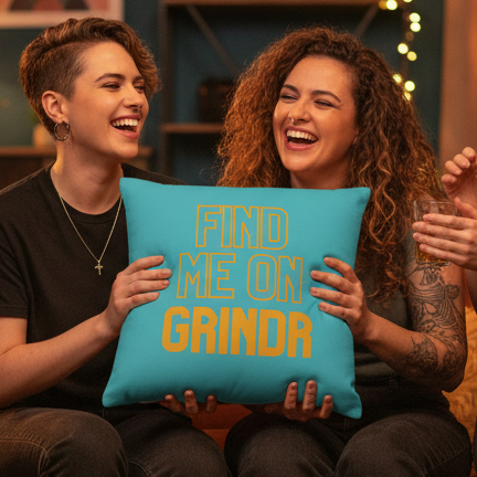 Two smiling people indoors hold a "Find Me On Grindr" pillow with bold yellow text, sharing a relaxed