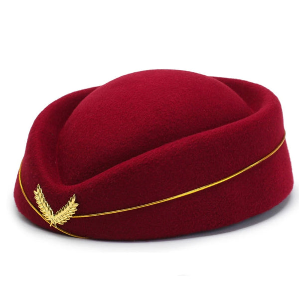 Front-left view of a burgundy pillbox-style hat with a gold trim cord and laurel brooch