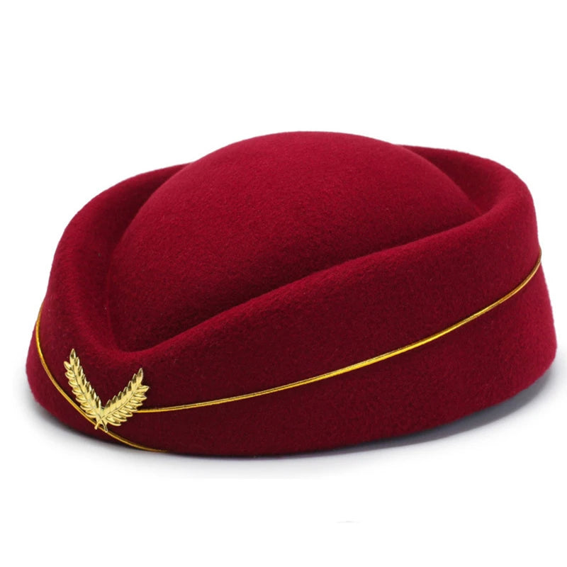 Front-left view of a burgundy pillbox-style hat with a gold trim cord and laurel brooch