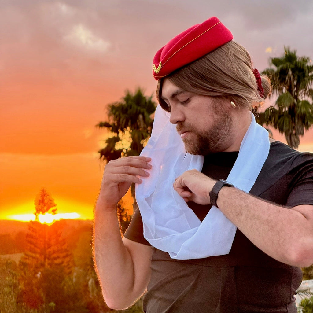 Person wearing a red pillbox hat and white scarf at sunset