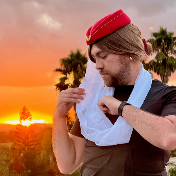 Person wearing a red pillbox hat and white scarf at sunset