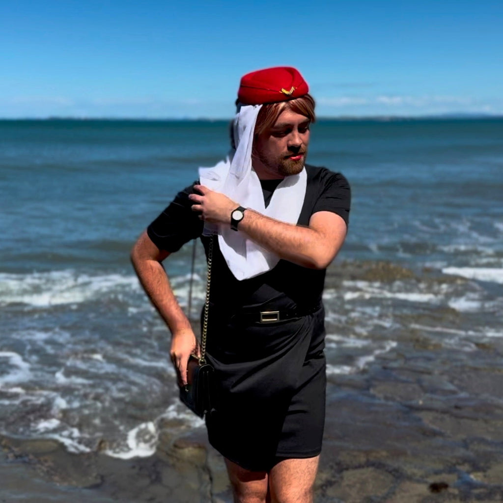 Bearded model wearing a red purser-style hat and white scarf by the ocean