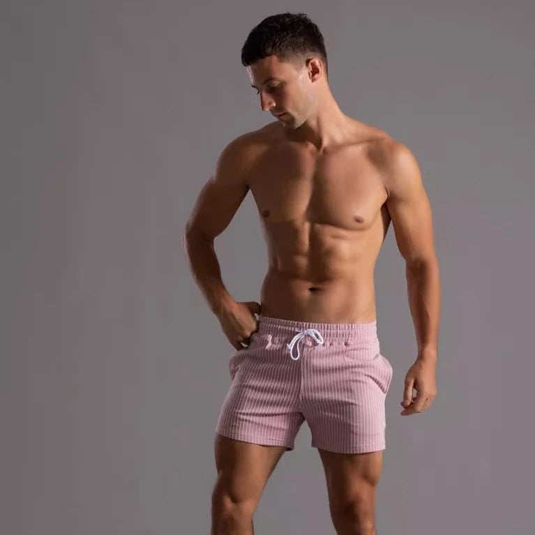 Front three-quarter view of a shirtless person wearing pink pinstriped drawstring shorts