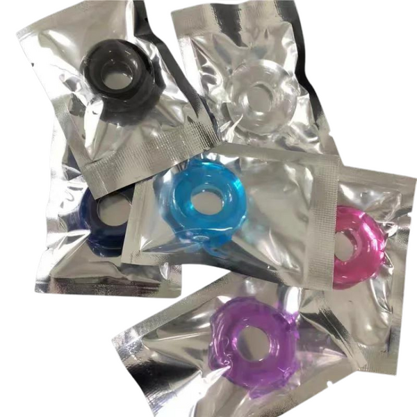Six colorful silicone penis rings individually sealed in silver packets, overlapping on white