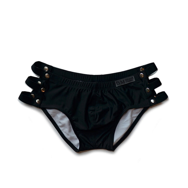 Front-facing black swim briefs with multiple side cutouts and metal studs, shown flat