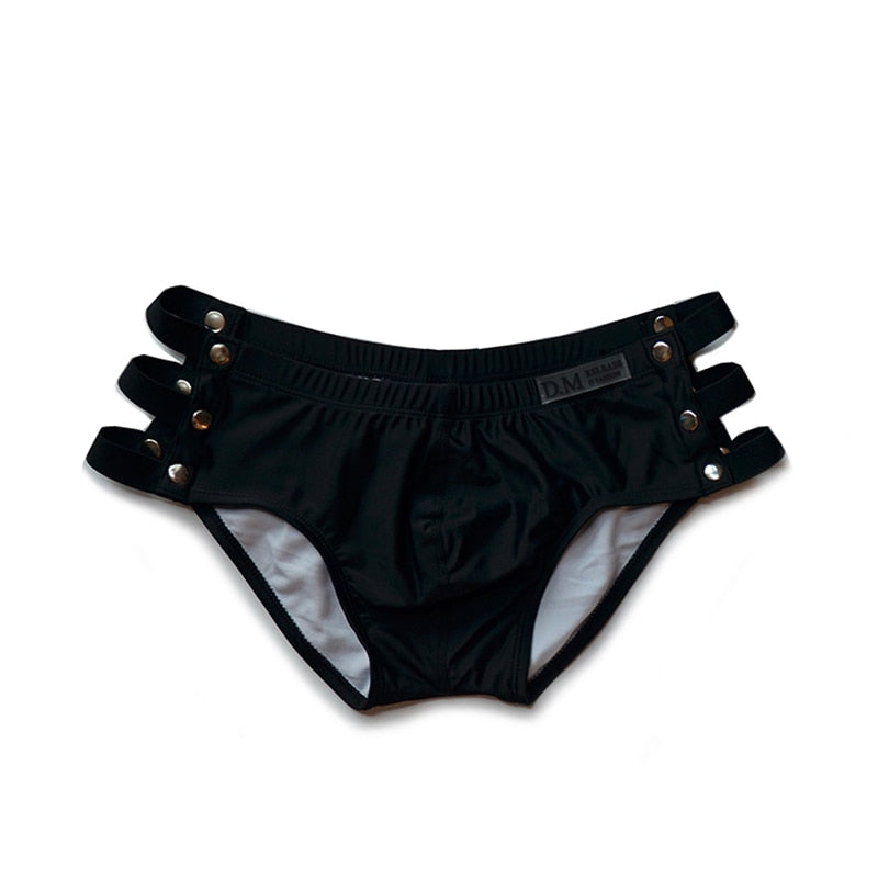 Front-facing black swim briefs with multiple side cutouts and metal studs, shown flat