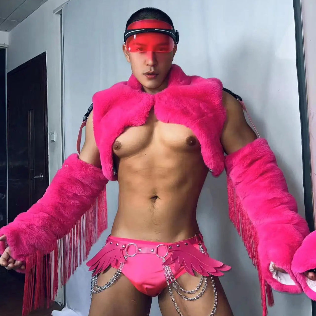 Front-facing model wearing a hot-pink faux-fur cropped shrug, briefs, and winged chain accessories