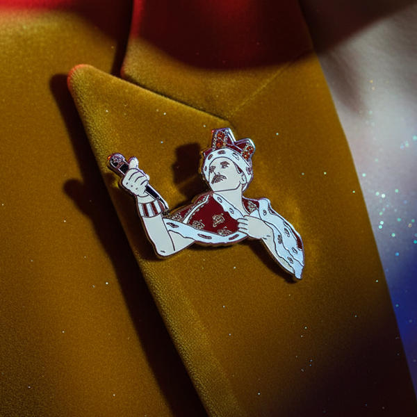 Close-up of a Freddie Mercury enamel pin showing him in a crown and holding a microphone