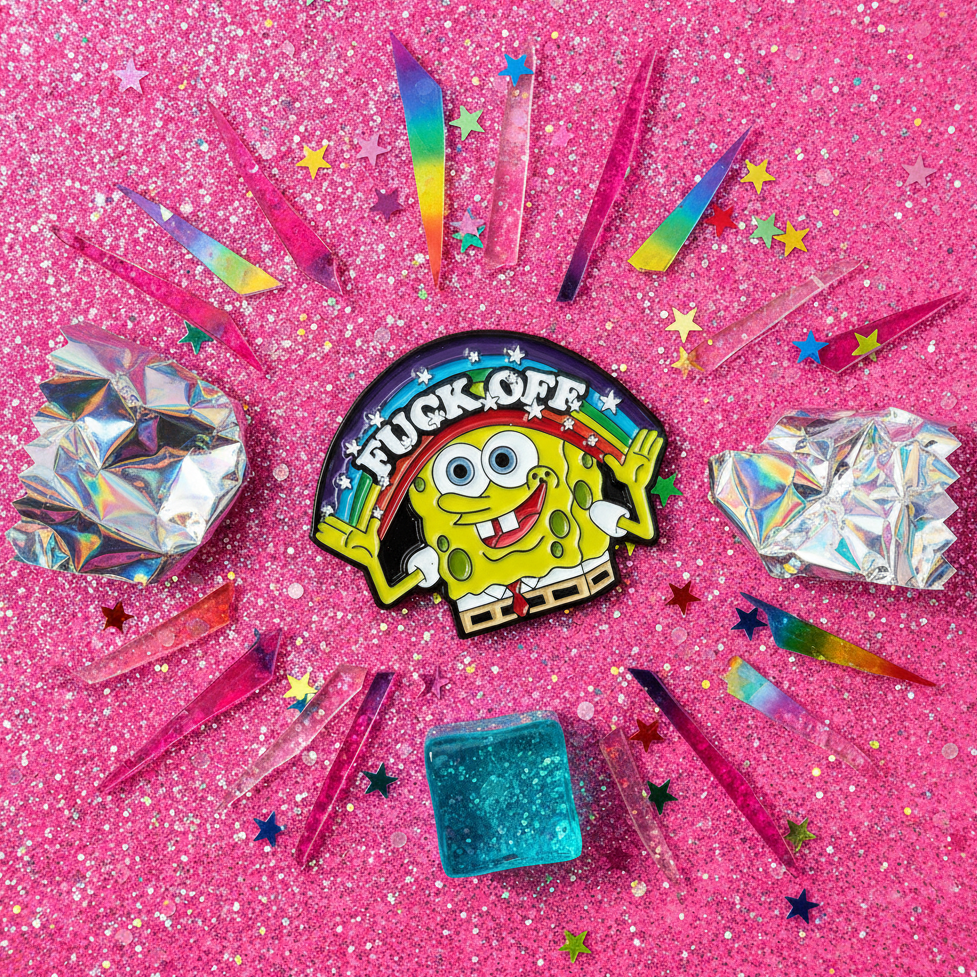 Close-up of a SpongeBob enamel pin reading “FUCK OFF,” with a rainbow and colorful star confetti