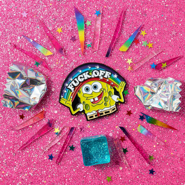 Close-up of a SpongeBob enamel pin reading “FUCK OFF,” with a rainbow and colorful star confetti