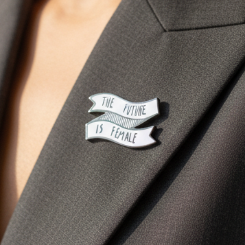 Close-up of a white enamel pin reading “THE FUTURE IS FEMALE” on a black lapel