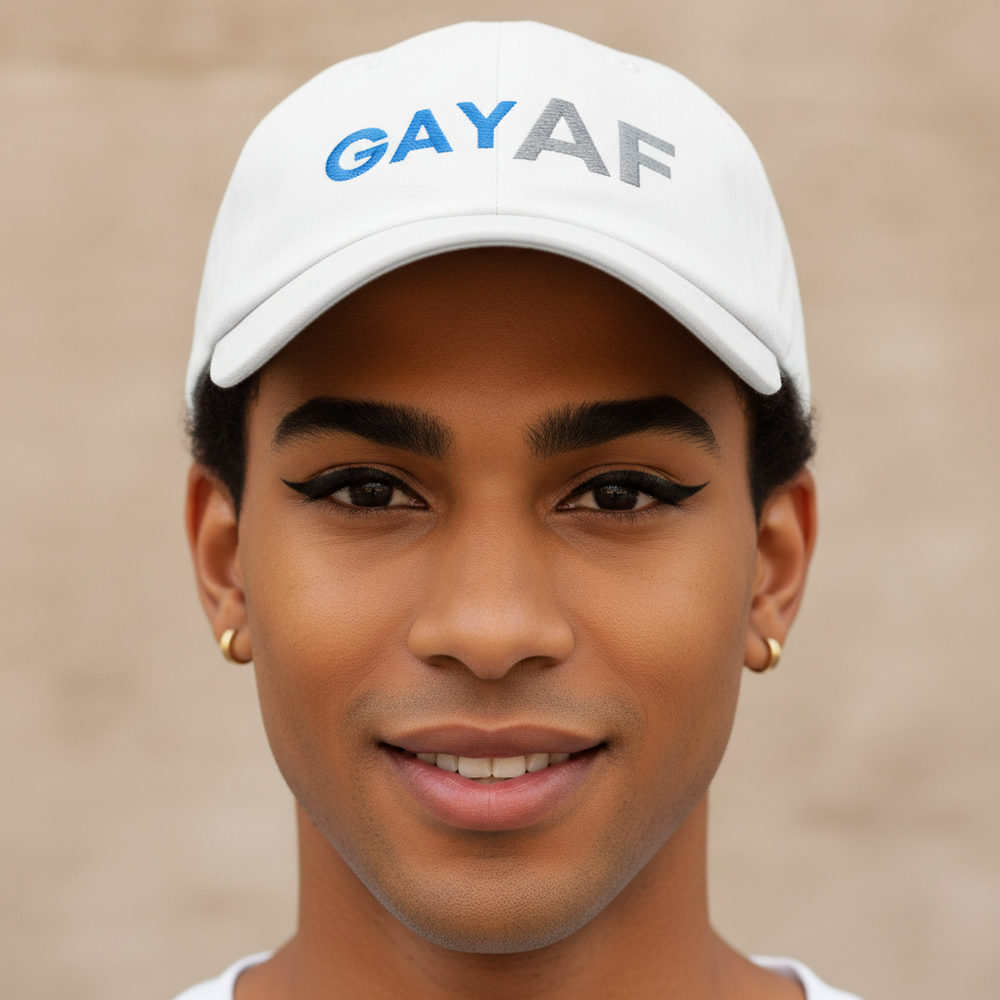 Gay AF Cap—a classic white hat with "GAY AF" embroidered in blue and gray—modeled by a young, dark-skinned queer person.