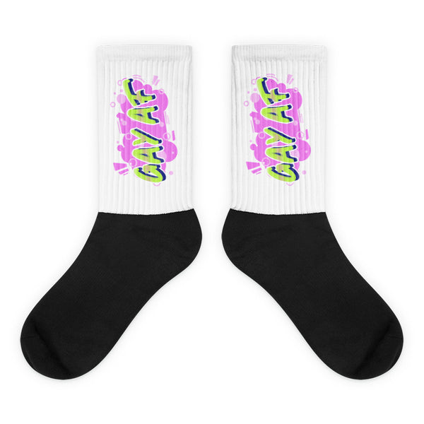 Pair of crew socks with black feet and white ribbed cuffs reading “GAY AF” in neon colors