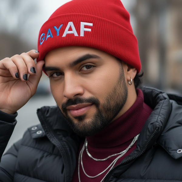Gay AF Cuffed Beanie worn by a bearded person with hoops, layered chains, black polish, black puffer, maroon top