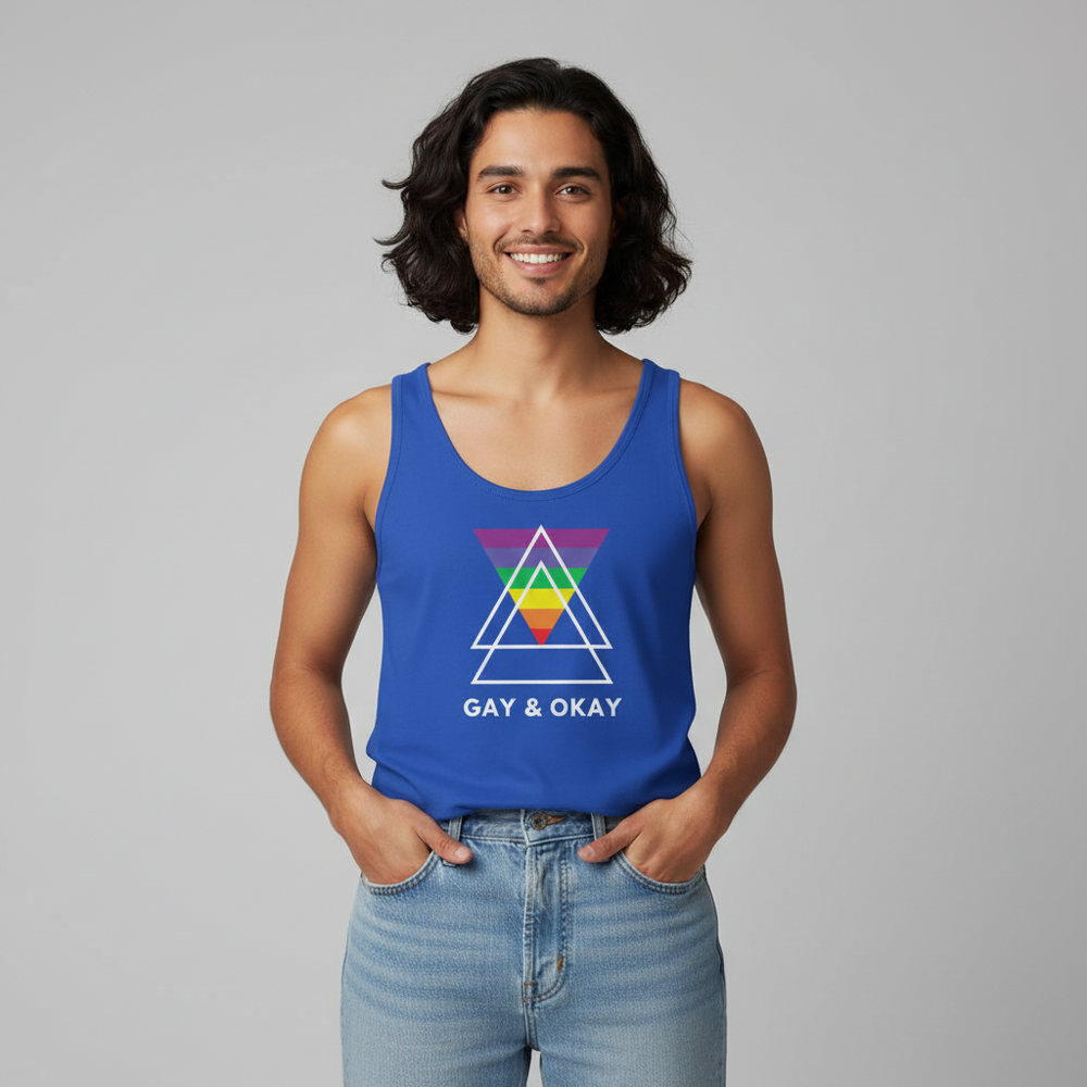 Unisex tank top with “GAY & OKAY” text and vibrant rainbow triangles, modeled by a queer person, hands in jeans pockets.