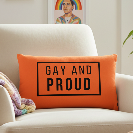 “Gay And Proud” pillow with bold black lettering on orange fabric, on beige armchair