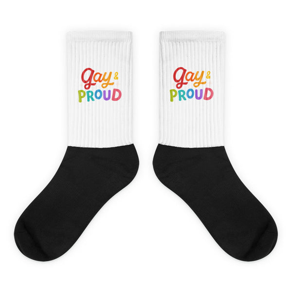 Pair of crew socks with white ribbed cuffs reading “Gay & Proud” over black feet