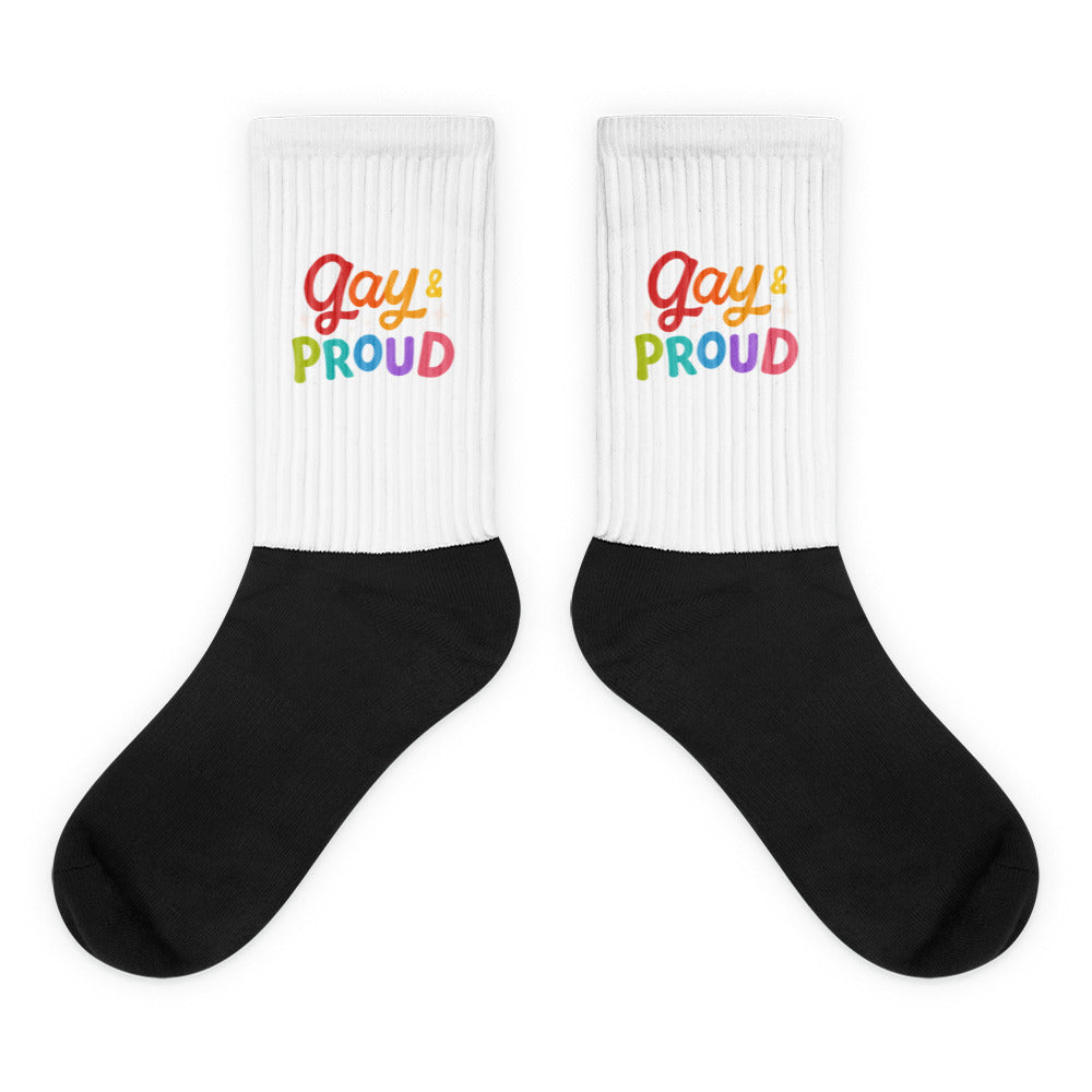 Pair of crew socks with white ribbed cuffs reading “Gay & Proud” over black feet