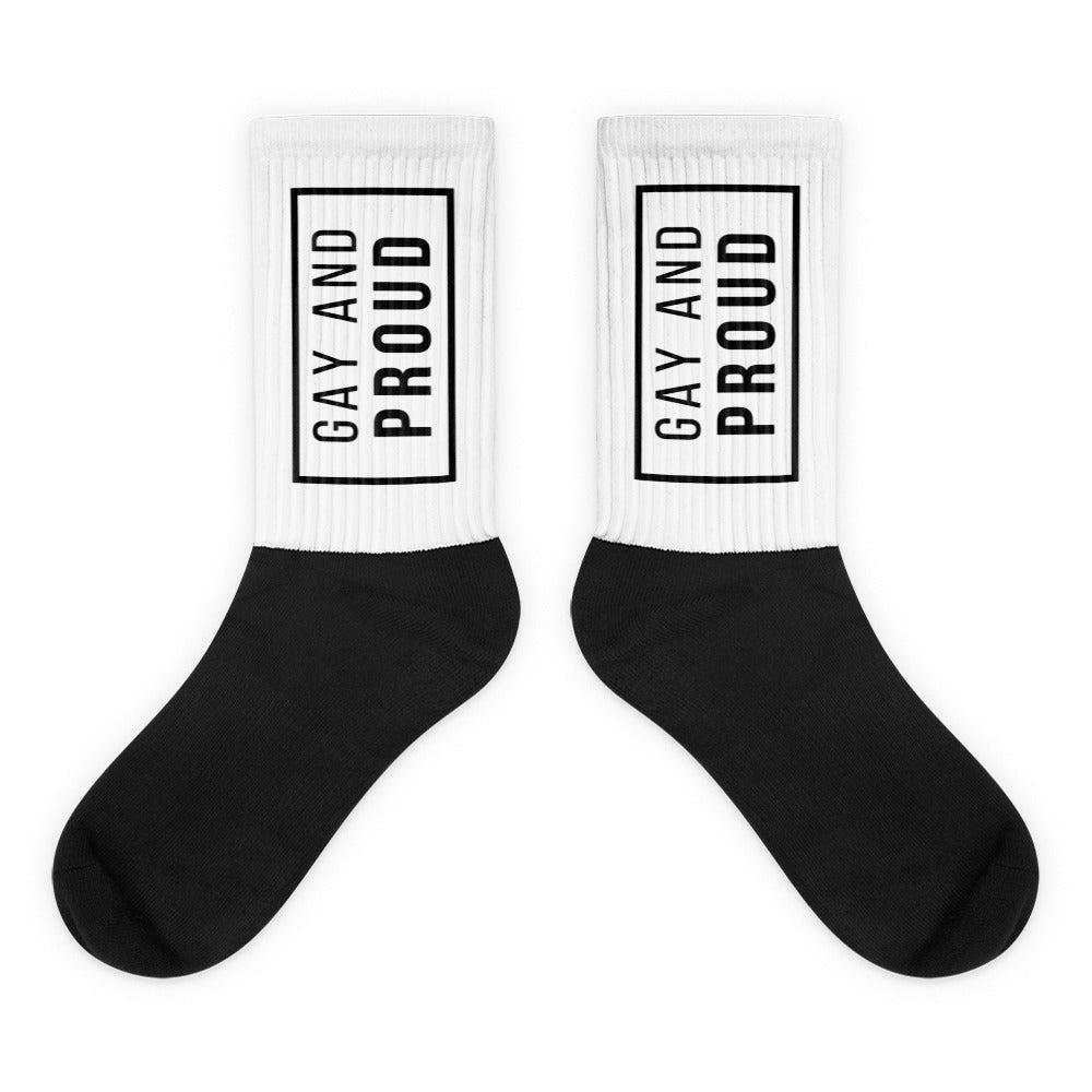 Pair of crew socks with white cuffs reading “GAY AND PROUD” and black feet