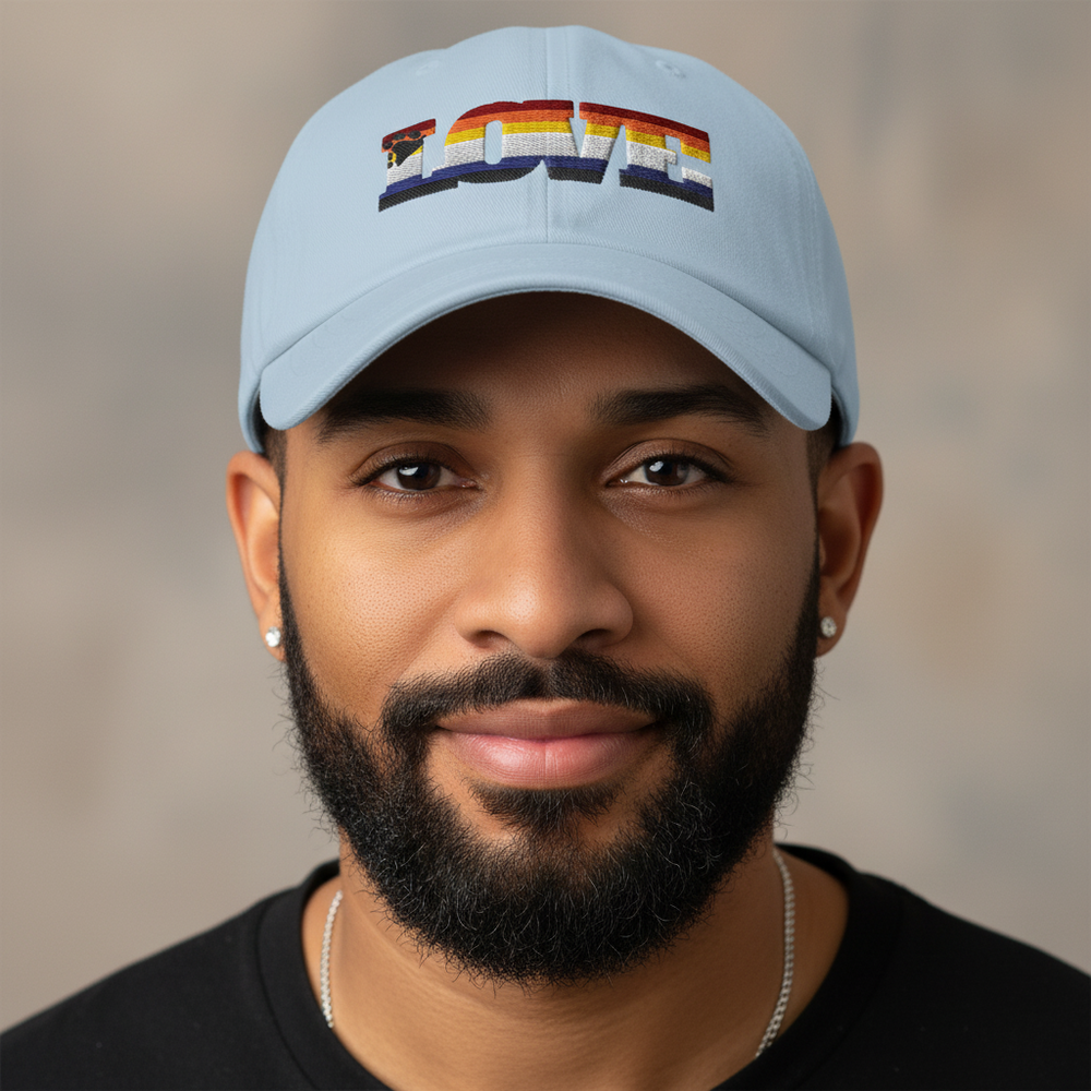 Light blue dad hat with "LOVE" in rainbow embroidery, worn by a smiling bearded man in black shirt; queer pride vibes.