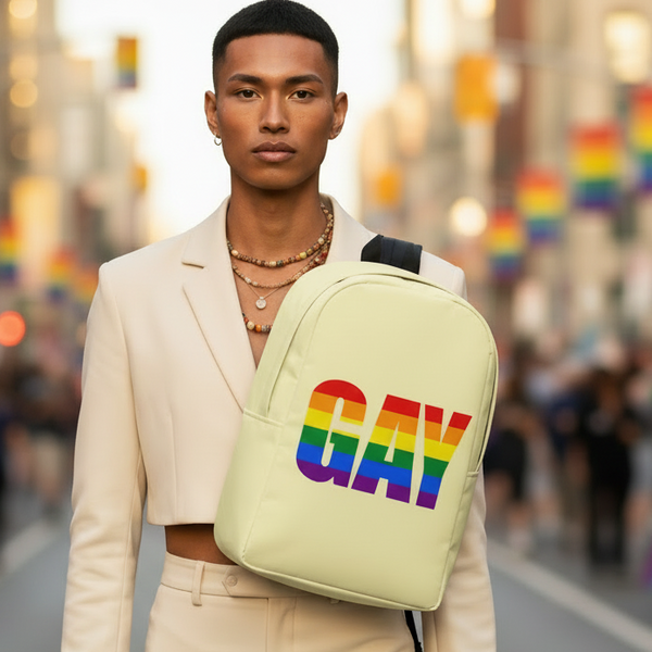 Front-facing model in a cream suit wearing a pale yellow backpack marked “GAY” in rainbow stripes