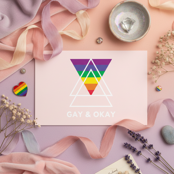 Queer postcard with “GAY & OKAY” over rainbow and white triangles, pastel pink-purple backdrop, plus dried flowers
