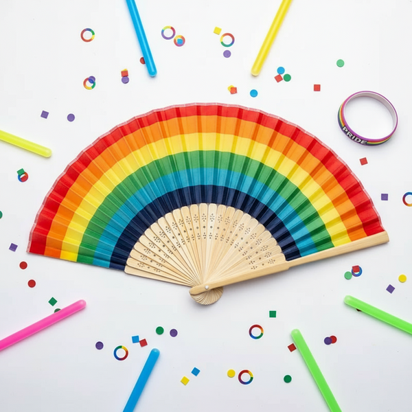 Open rainbow-striped hand fan with light wood ribs on a confetti-strewn white surface