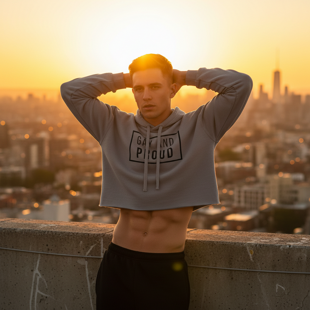 The Gay And Proud Crop Hoodie pops against black pants as a young man models carefree queer vibes on a sunset city rooftop.