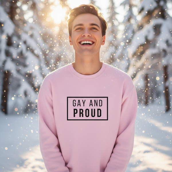 Smiling person in a snowy forest wearing a pink sweatshirt reading “GAY AND PROUD”