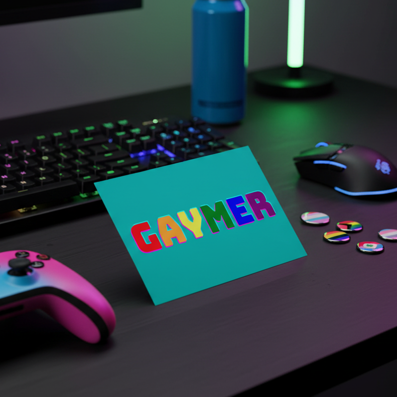 Gaymer postcard: teal, with bold rainbow "GAYMER" text, on a gaming desk with rainbow-lit keyboard, pins, and pride vibes.